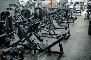 Gym interior with various exercise machines arranged in rows.